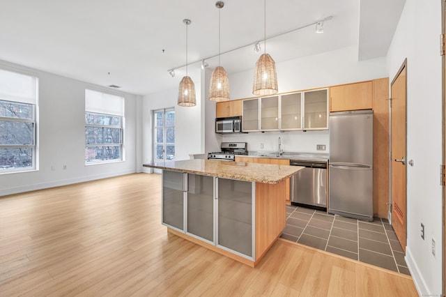 kitchen with sink, stainless steel appliances, light stone countertops, decorative light fixtures, and light wood-type flooring