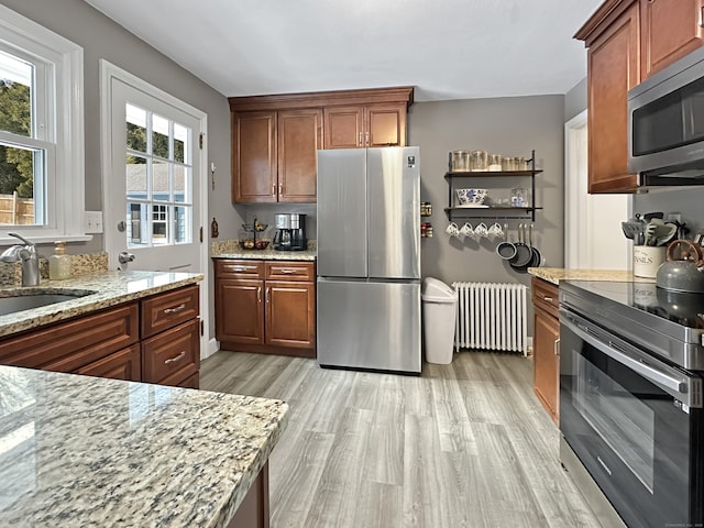 kitchen with sink, light stone counters, light hardwood / wood-style flooring, appliances with stainless steel finishes, and radiator heating unit