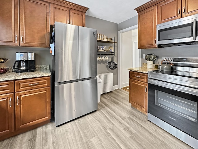 kitchen with stainless steel appliances, light stone countertops, radiator heating unit, and light hardwood / wood-style flooring