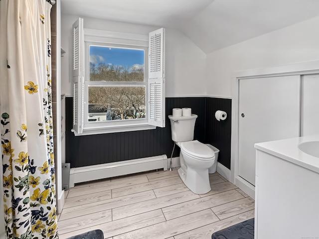 bathroom with lofted ceiling, hardwood / wood-style flooring, baseboard heating, vanity, and toilet