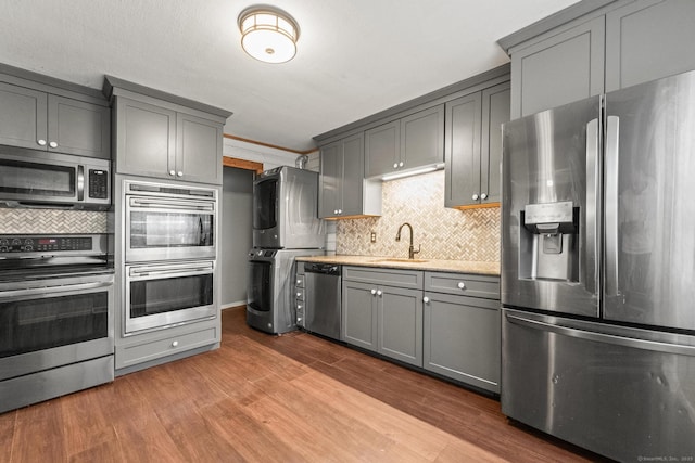 kitchen with gray cabinets, sink, hardwood / wood-style flooring, stacked washer and dryer, and stainless steel appliances