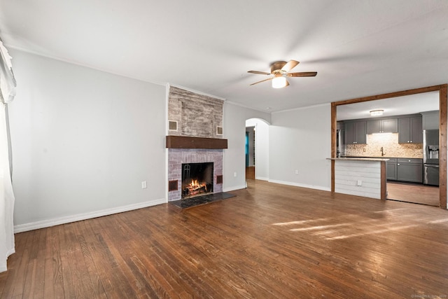 unfurnished living room with sink, a large fireplace, dark hardwood / wood-style floors, and ceiling fan