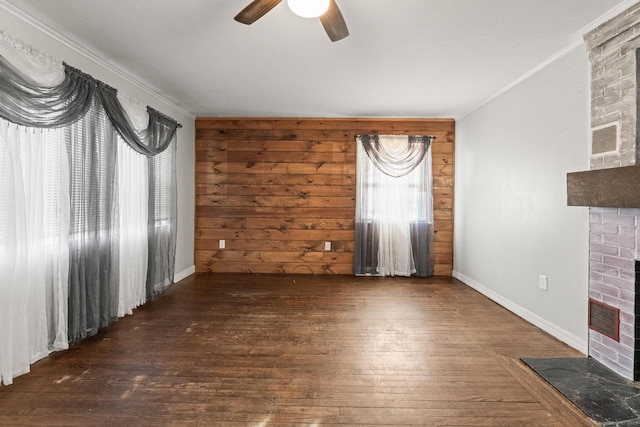 unfurnished living room featuring wooden walls, ornamental molding, ceiling fan, a brick fireplace, and dark wood-type flooring