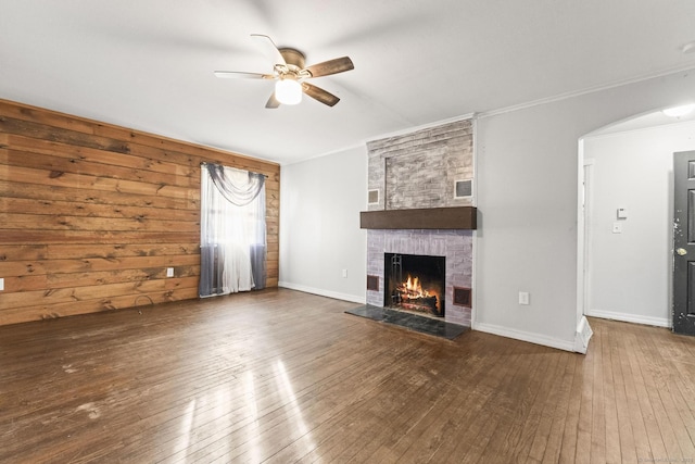 unfurnished living room with a brick fireplace, wood-type flooring, ornamental molding, and ceiling fan