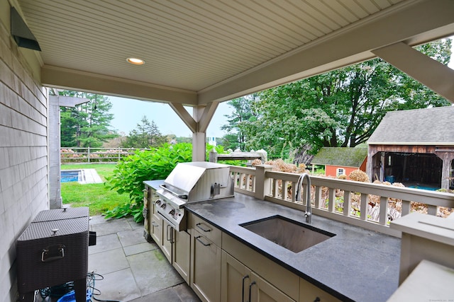 view of patio with an outdoor kitchen, an outbuilding, a grill, fence, and a sink