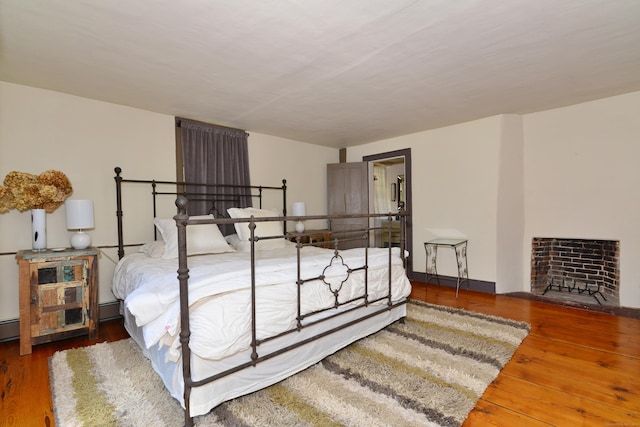 bedroom featuring dark wood-type flooring, baseboard heating, and a fireplace