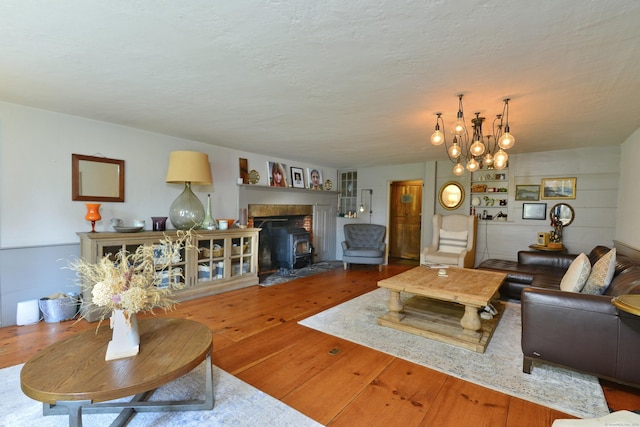 living room featuring a textured ceiling, wood-type flooring, a wood stove, and a notable chandelier