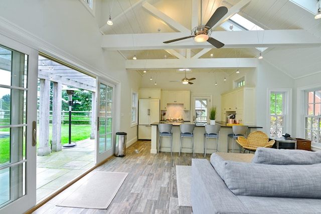 living area featuring light wood finished floors, ceiling fan, high vaulted ceiling, beamed ceiling, and baseboards