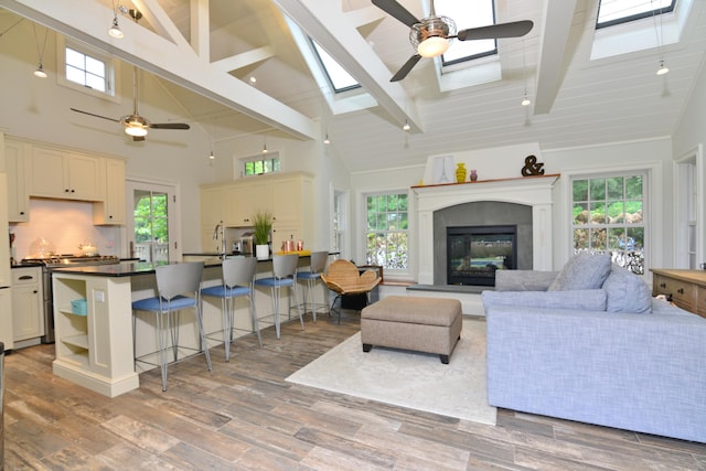 living area featuring a skylight, wood finished floors, beam ceiling, plenty of natural light, and a glass covered fireplace