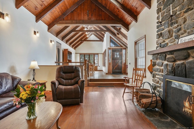 living room featuring a stone fireplace, high vaulted ceiling, wood-type flooring, wood ceiling, and beam ceiling