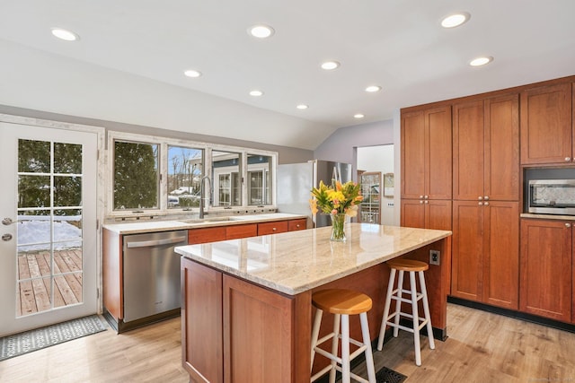 kitchen featuring sink, light wood-type flooring, appliances with stainless steel finishes, a kitchen island, and light stone countertops