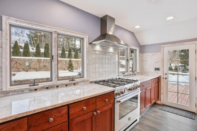 kitchen featuring high end stainless steel range oven, backsplash, island range hood, light stone countertops, and vaulted ceiling