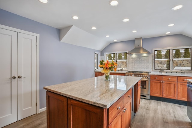 kitchen featuring wall chimney exhaust hood, vaulted ceiling, appliances with stainless steel finishes, a kitchen island, and light stone countertops