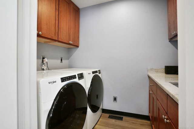 laundry area with cabinets, separate washer and dryer, and light hardwood / wood-style flooring