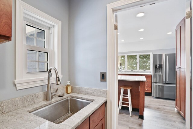 kitchen with sink, a kitchen breakfast bar, stainless steel fridge with ice dispenser, light stone countertops, and light wood-type flooring