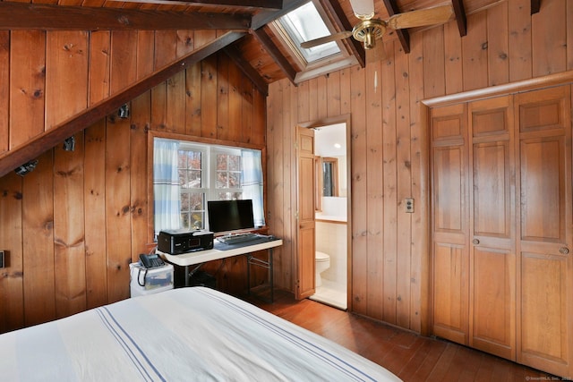 bedroom featuring dark wood-type flooring, lofted ceiling with skylight, ensuite bathroom, and wood walls