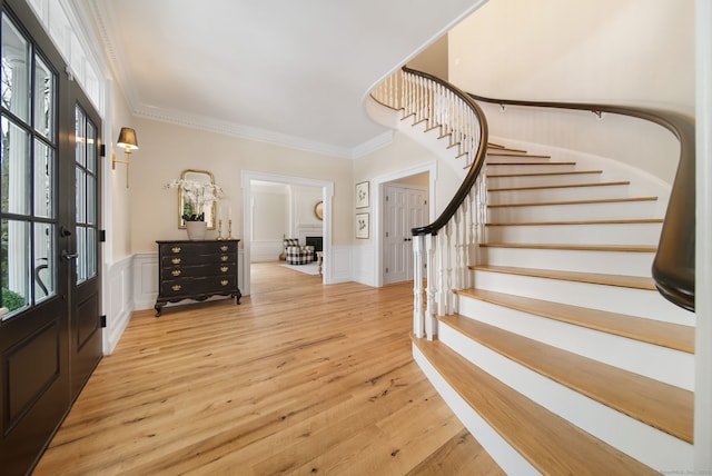 foyer entrance featuring light wood-type flooring, wainscoting, crown molding, and stairway