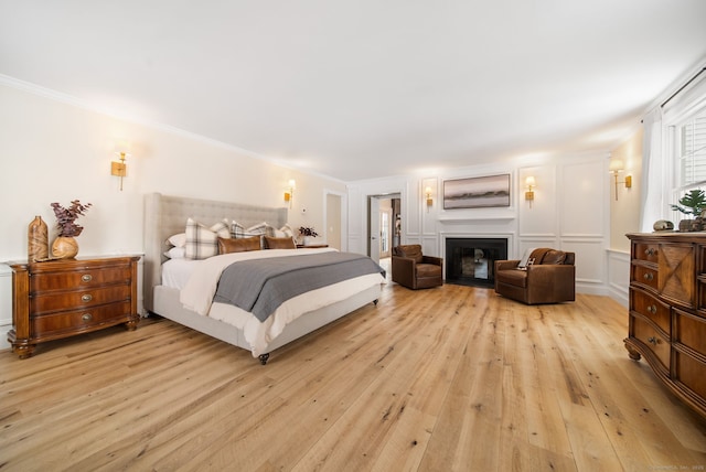 bedroom featuring light wood-style floors, a fireplace, a decorative wall, and crown molding