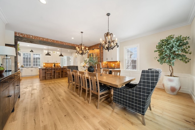 dining area with a wainscoted wall, light wood finished floors, ornamental molding, and a decorative wall