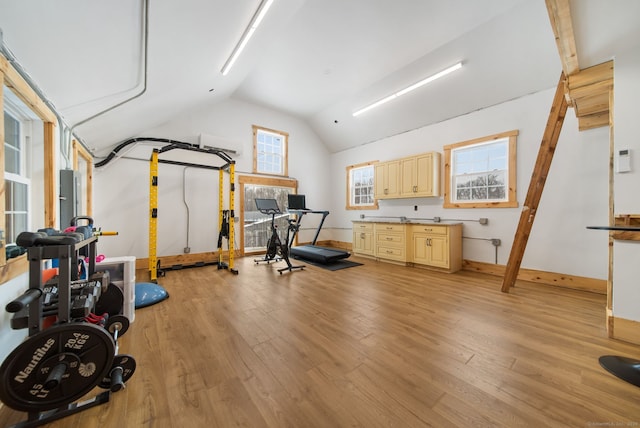 exercise room featuring lofted ceiling, light wood finished floors, and baseboards