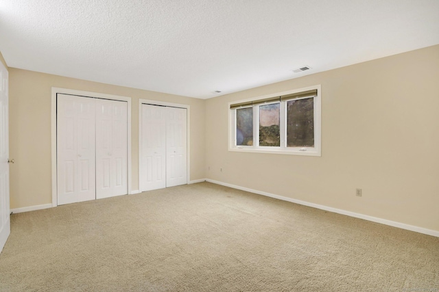 unfurnished bedroom with a textured ceiling, carpet floors, and multiple closets