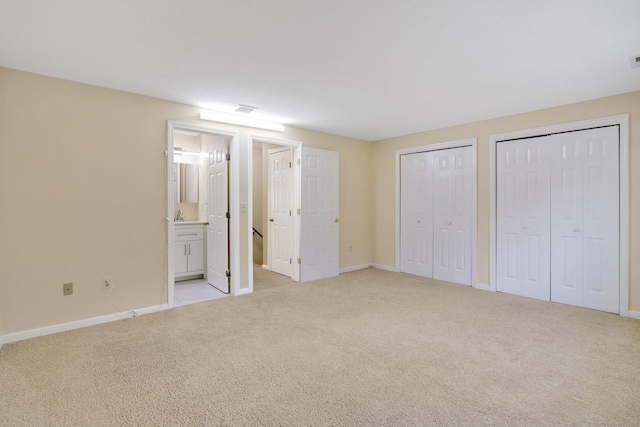 unfurnished bedroom with multiple closets, ensuite bathroom, and light carpet