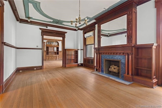 unfurnished living room featuring a wall unit AC, ornamental molding, light hardwood / wood-style floors, a tiled fireplace, and a chandelier