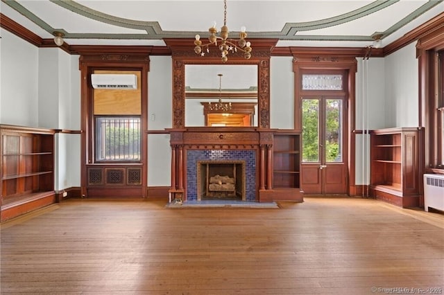 unfurnished living room with crown molding, a wall unit AC, a tiled fireplace, a chandelier, and light wood-type flooring