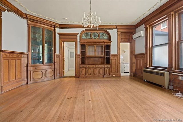 unfurnished living room with light hardwood / wood-style flooring, an inviting chandelier, radiator heating unit, a wall mounted air conditioner, and ornamental molding