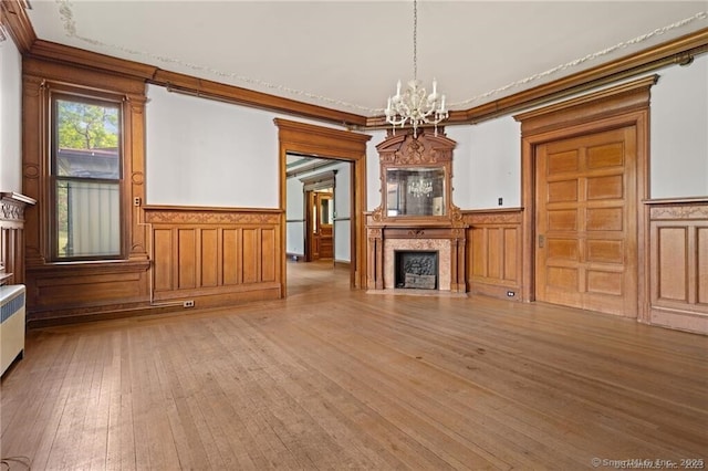 unfurnished living room with an inviting chandelier, light wood-type flooring, ornamental molding, radiator heating unit, and a high end fireplace