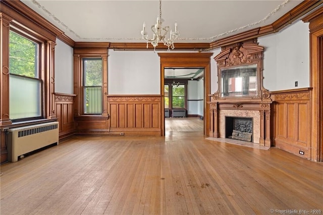 unfurnished living room with an inviting chandelier, crown molding, light hardwood / wood-style flooring, radiator heating unit, and a fireplace