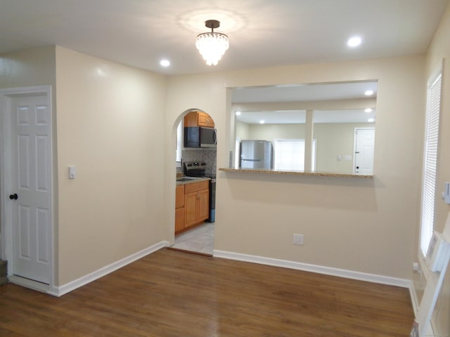 kitchen with appliances with stainless steel finishes, hardwood / wood-style floors, decorative backsplash, light stone counters, and kitchen peninsula