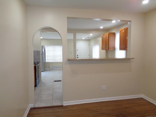 kitchen featuring light stone counters, light hardwood / wood-style flooring, kitchen peninsula, and baseboard heating