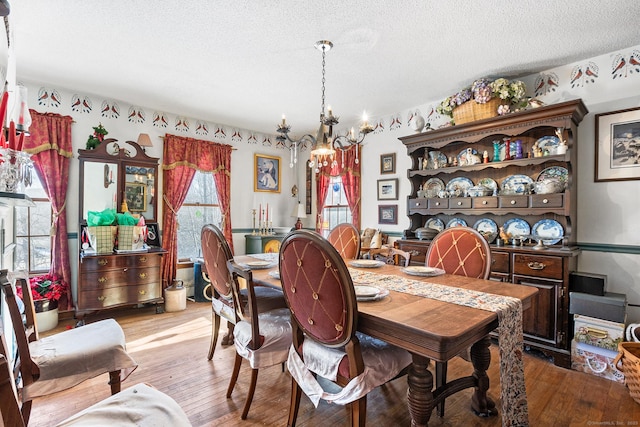 dining area with light hardwood / wood-style floors, a textured ceiling, and a notable chandelier