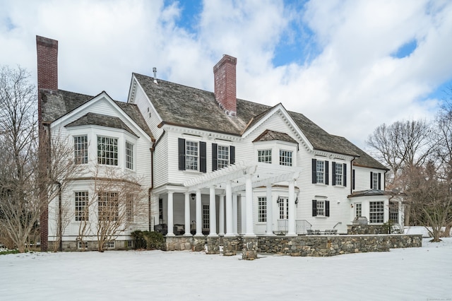 snow covered rear of property featuring a chimney and a pergola