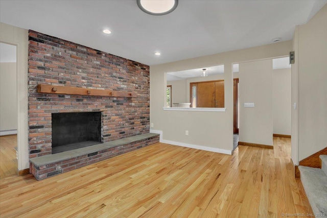 unfurnished living room with a baseboard radiator, a brick fireplace, and light hardwood / wood-style flooring