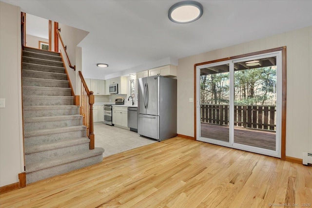 kitchen with sink, appliances with stainless steel finishes, white cabinets, light hardwood / wood-style floors, and a baseboard heating unit