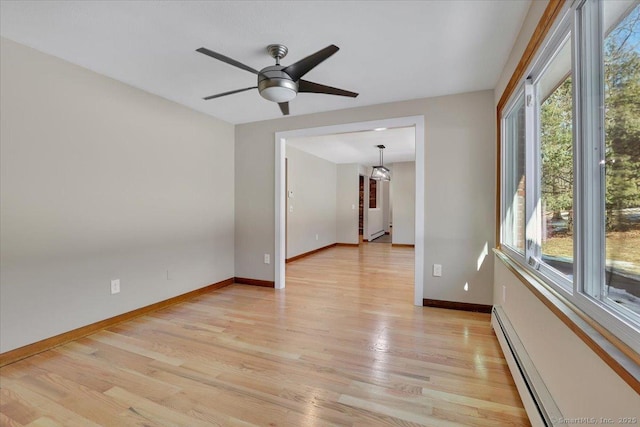 spare room with a baseboard heating unit, a healthy amount of sunlight, and light wood-type flooring