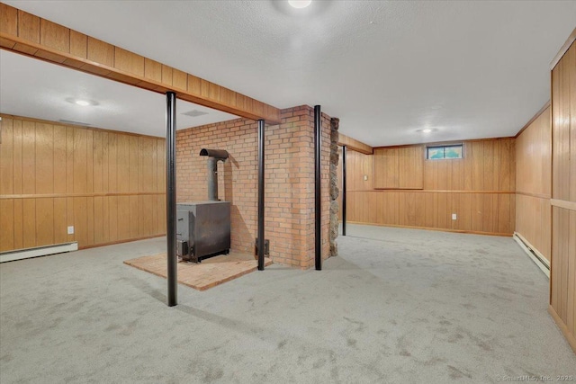 basement featuring wood walls, a wood stove, light colored carpet, baseboard heating, and a textured ceiling