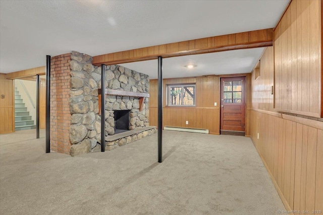 unfurnished living room with a stone fireplace, wooden walls, baseboard heating, light carpet, and a textured ceiling