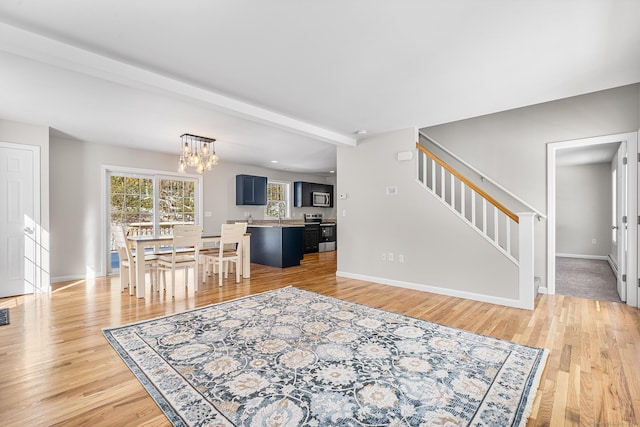 living area with beamed ceiling, stairway, light wood-style flooring, and baseboards