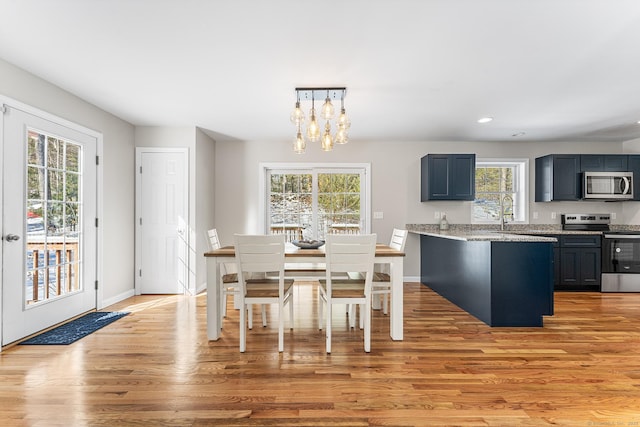 kitchen featuring a chandelier, light stone counters, light wood-style floors, appliances with stainless steel finishes, and decorative light fixtures