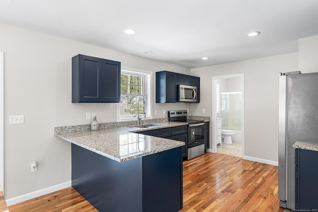 kitchen with a peninsula, blue cabinets, stainless steel appliances, a kitchen bar, and a sink