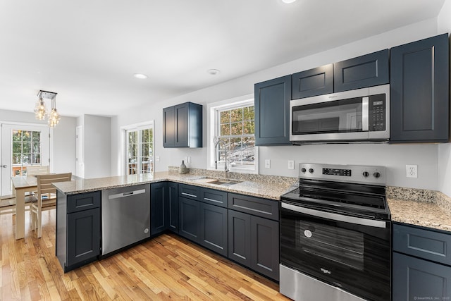 kitchen featuring stainless steel appliances, light wood-style floors, a sink, and light stone counters