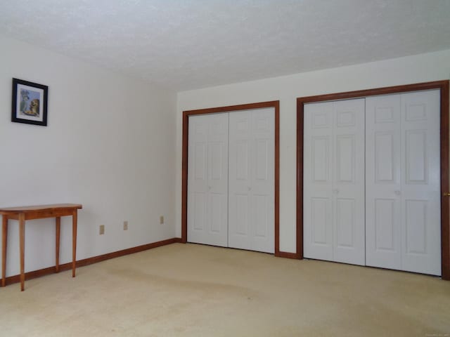 unfurnished bedroom with multiple closets, light colored carpet, and a textured ceiling