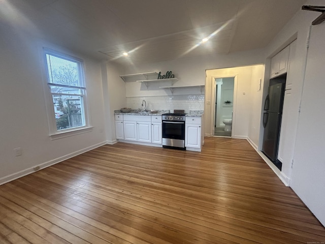 kitchen featuring sink, stainless steel stove, light hardwood / wood-style flooring, black refrigerator, and white cabinets