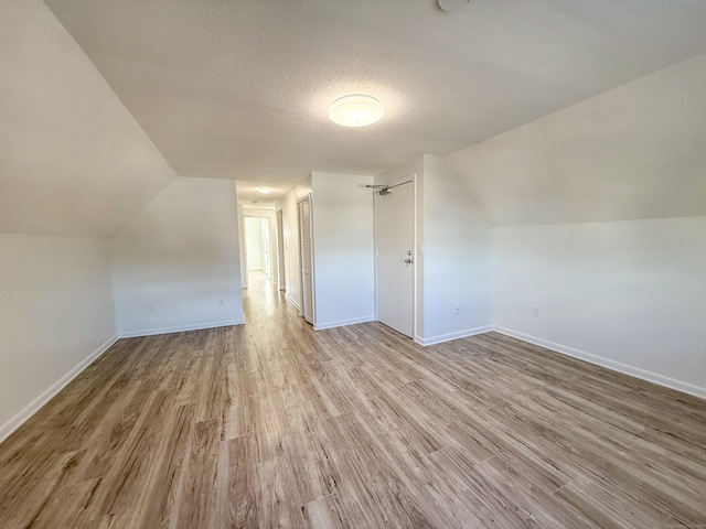 additional living space featuring lofted ceiling, a textured ceiling, and light wood-type flooring