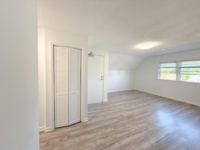 additional living space featuring vaulted ceiling, a textured ceiling, and light hardwood / wood-style floors