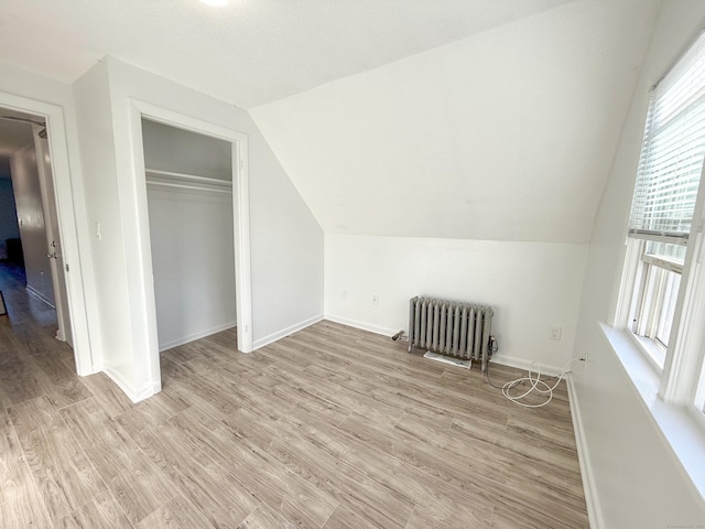 additional living space featuring lofted ceiling, radiator heating unit, and light wood-type flooring