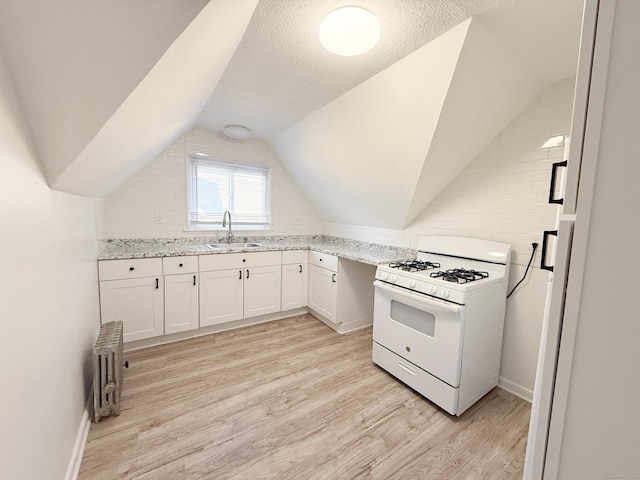 kitchen with vaulted ceiling, white cabinetry, sink, light hardwood / wood-style floors, and white gas range oven